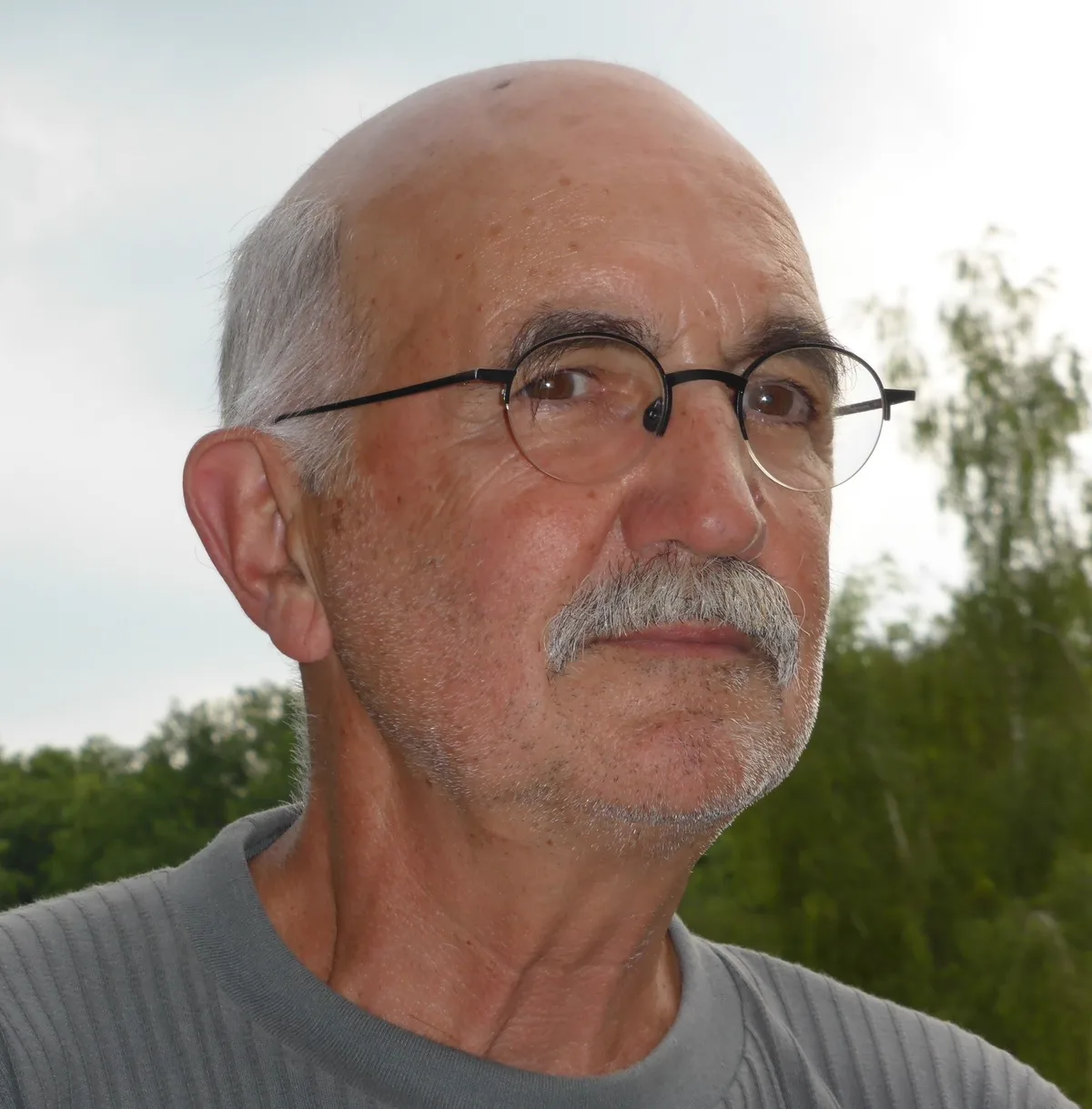 Ein Mann mit Brille und grauem T-Shirt guckt in die Ferne.